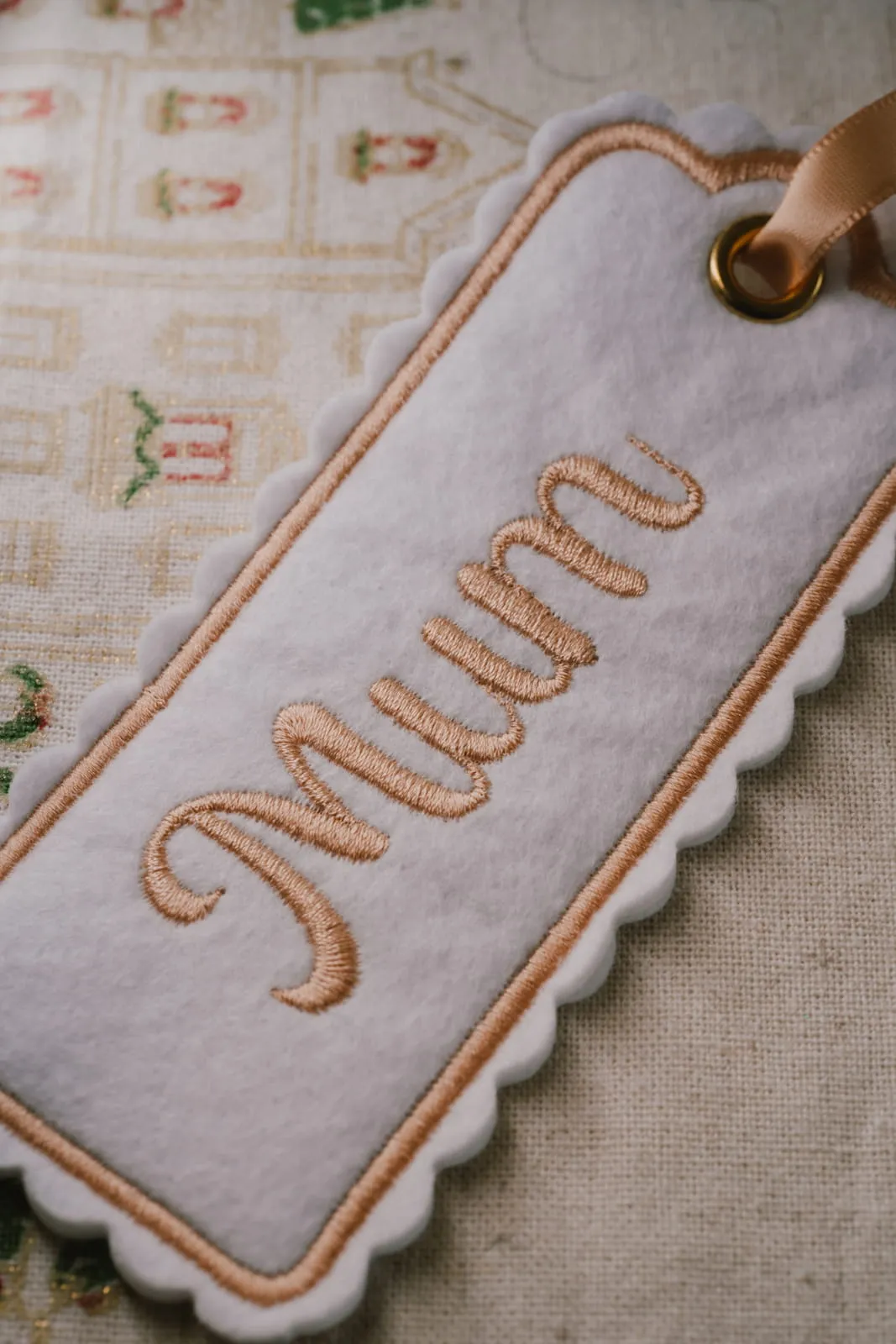 Close-up of an embroidered felt gift tag reading Mum with a scalloped border and ribbon