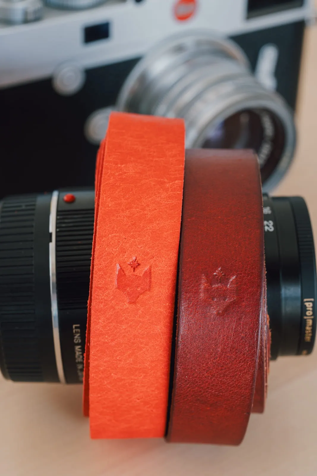 Two orange and red leather camera straps with embossed logo resting on a vintage film camera