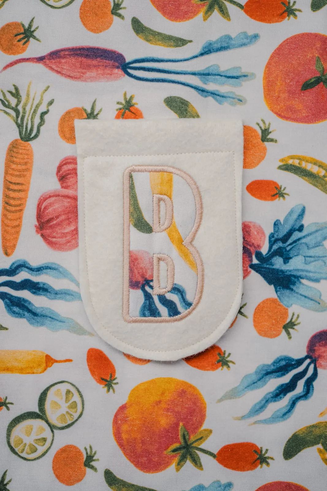 Felt pocket featuring a colourful embroidered letter B on a vibrant vegetable-print fabric background