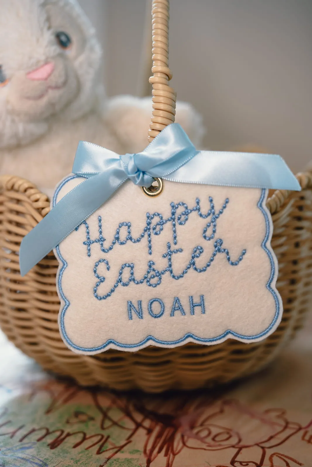 Personalised Happy Easter Noah embroidered felt tag with blue ribbon on a wicker Easter basket surrounded by chocolates