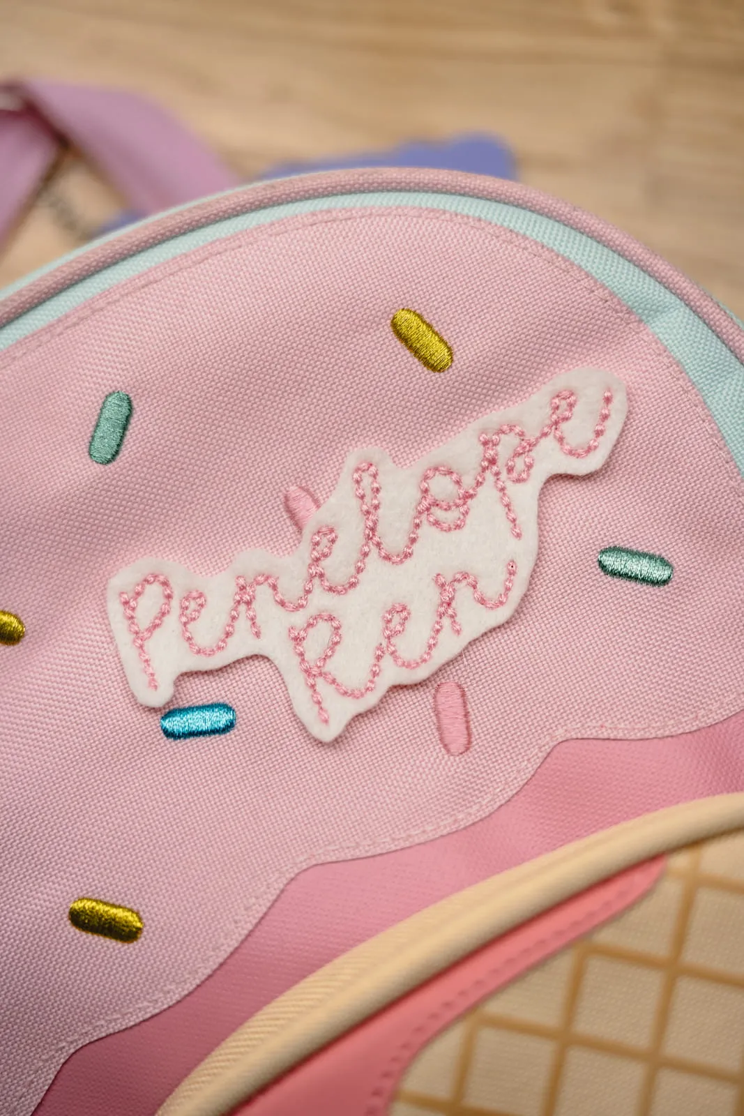 Pink donut-shaped backpack with a personalised Penelope Fea embroidered name patch with colourful sprinkle details