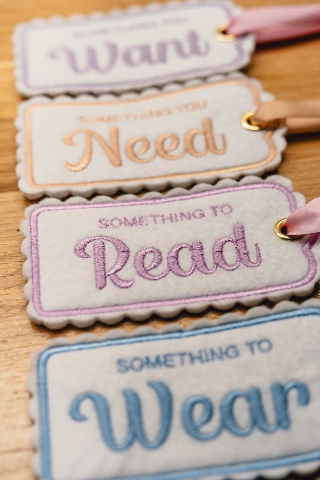 Four embroidered felt gift tags in pastel colours — Want, Need, Read, Wear — arranged on a warm wooden surface